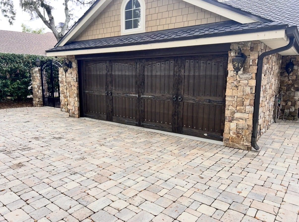 Dark carriage house style garage door with decorative hardware between stone columns, installed by Just-In-Time Garage Door