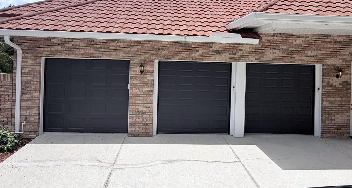 Three matching black raised panel garage doors on a brick home with a tile roof